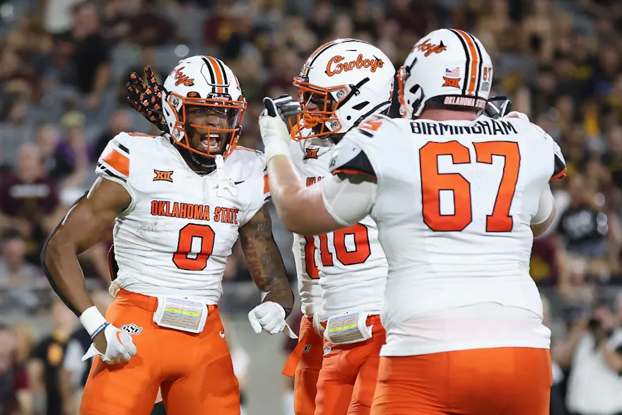Running back Ollie Gordon II of the Oklahoma State Cowboys celebrates with Cole Birmingham after scoring on a two-yard rushing touchdown against the Arizona State Sun Devils as we look at our Caesars promo code for Texas A&M-Oklahoma State.