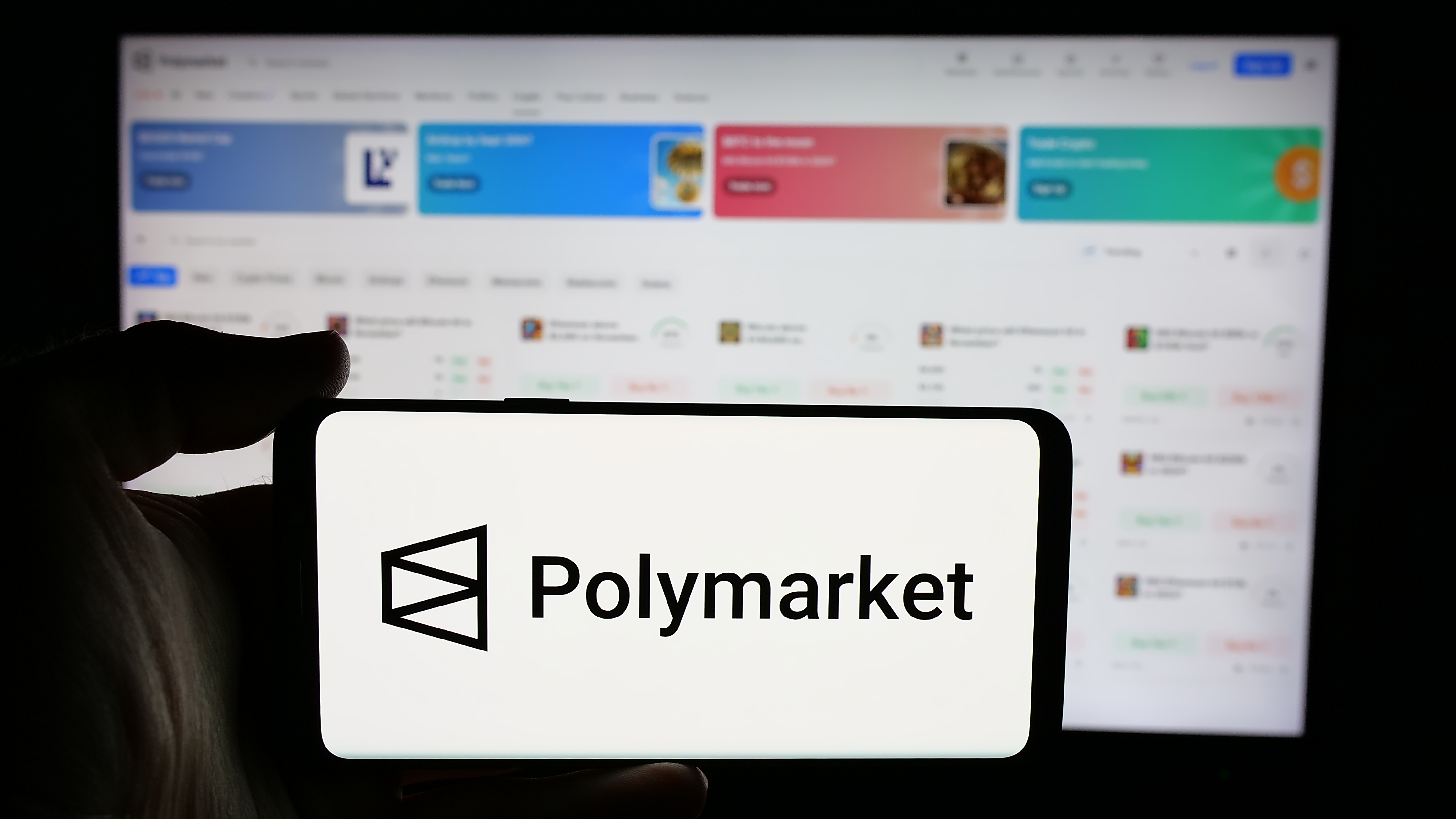 A person is holding a cellphone with the logo of Polymarket as we look at the company's reentry into the US market.