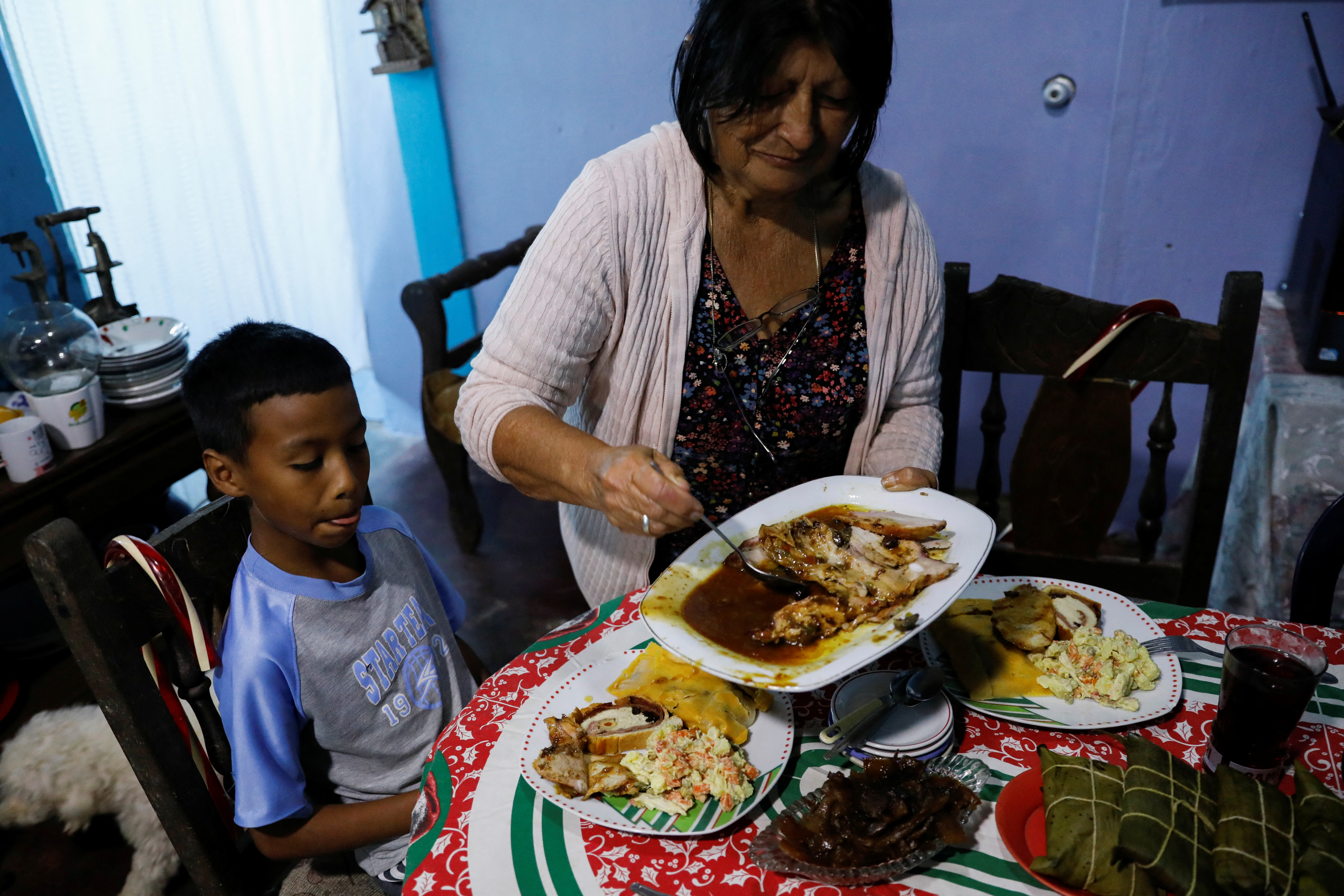 Gladys de Chavez, 69, serves her great-grandson a portion of the typical pork leg “pernil” as they prepare Christmas dinner with her family.