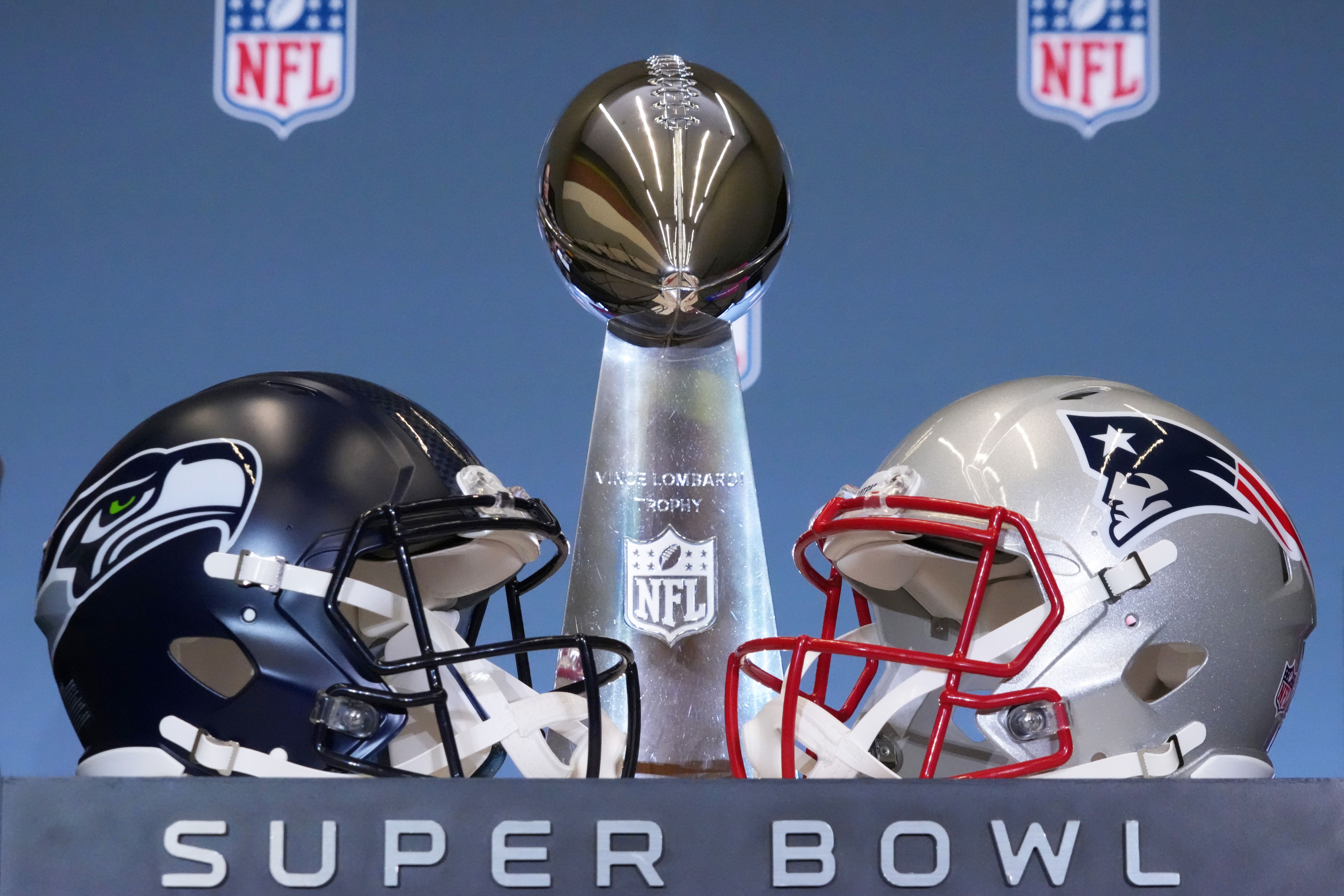 The Seattle Seahawks and New England Patriots helmets are displayed with the Vince Lombardi Trophy as we break down our Super Bowl AI prediction.