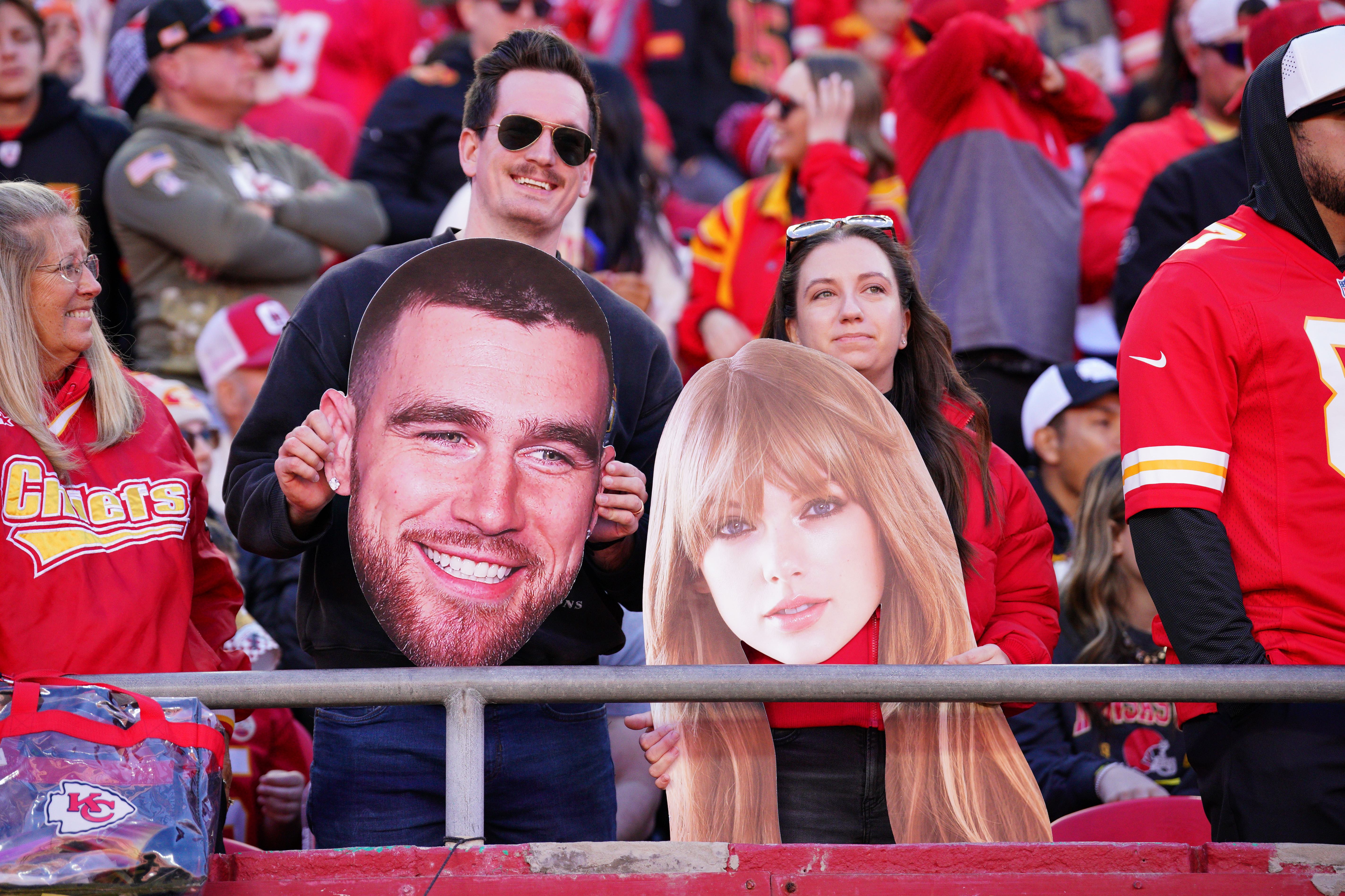 Kansas City Chiefs fans hold fathead signs of Travis Kelce and Taylor Swift as we break down the best Travis Kelce player props based on Swift's attendance.
