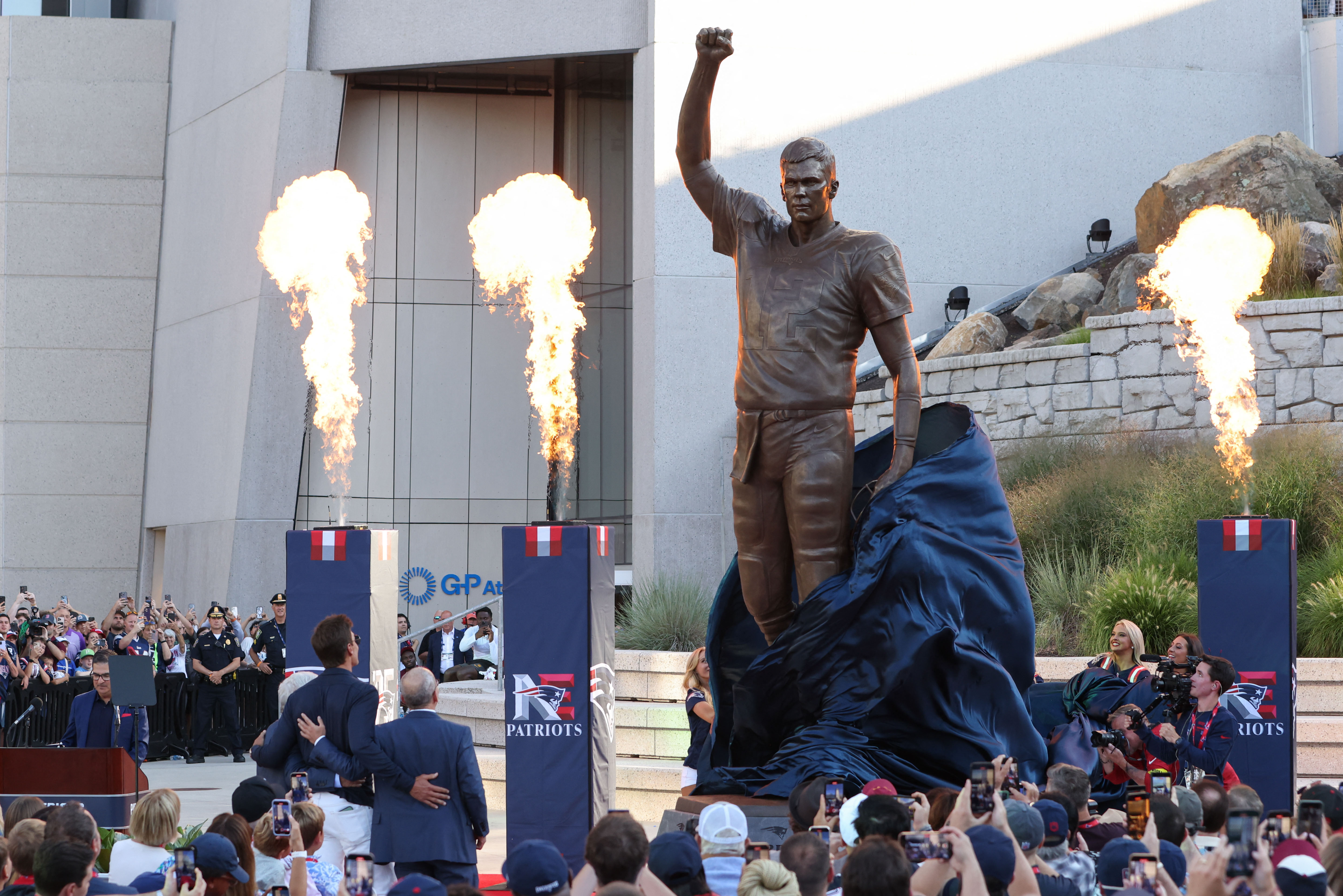 Retired New England Patriot Hall of Famer Tom Brady stands with Jonathan and Robert Kraft during a statue unveiling as we look at who he's cheering for in today's Super Bowl.