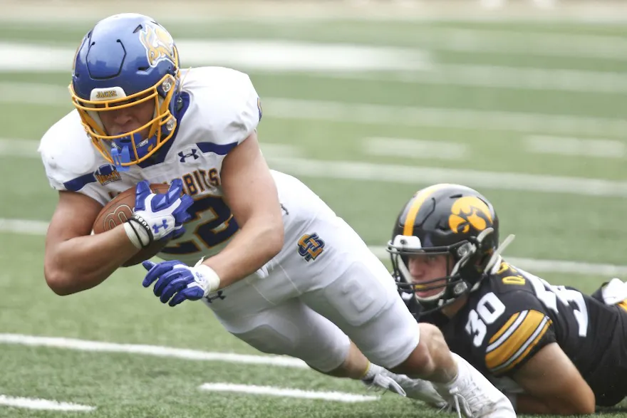 Running back Isaiah Davis of the South Dakota State Jackrabbits is tripped up as he carries the ball against the Iowa Hawkeyes, and we offer our top Montana vs. South Dakota State prediction based on the best NCAAF odds.