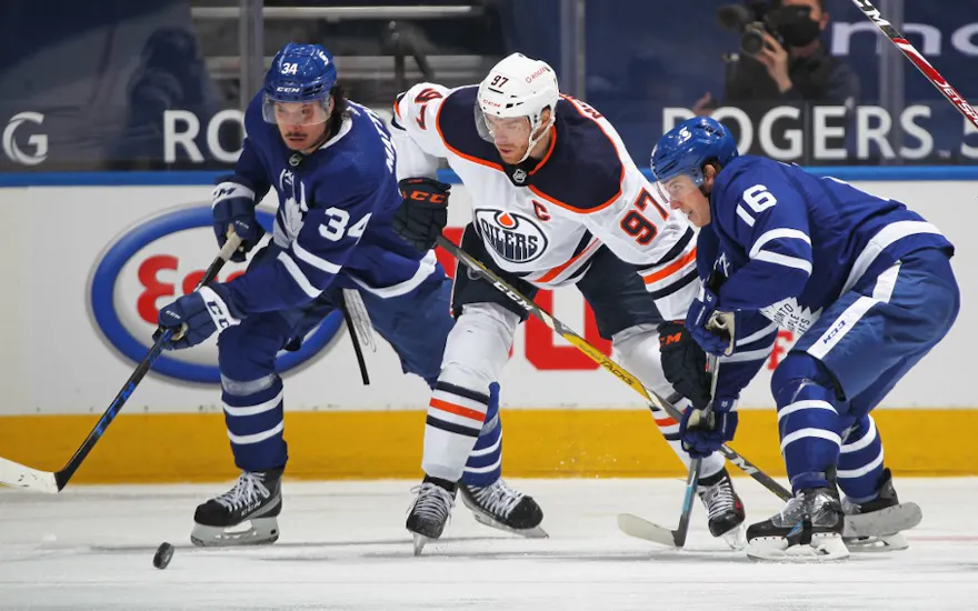 Connor McDavid of the Edmonton Oilers battles for the puck between Auston Matthews and Mitchell Marner of the Toronto Maple Leafs.