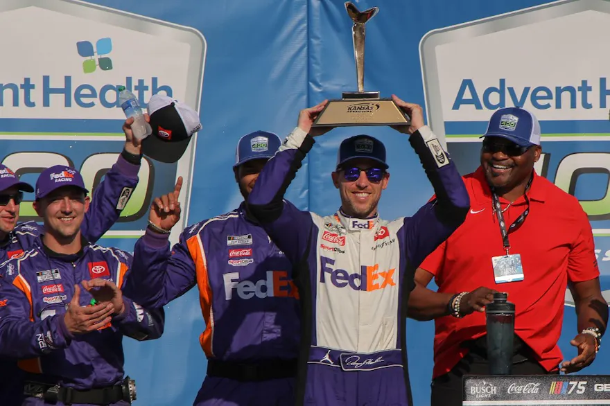 Denny Hamlin, driver of the No. 11 FedEx Express Toyota, lifts the Kansas Speedway trophy in victory lane as we preview the 2024 AdventHealth 400 at Kansas Speedway.