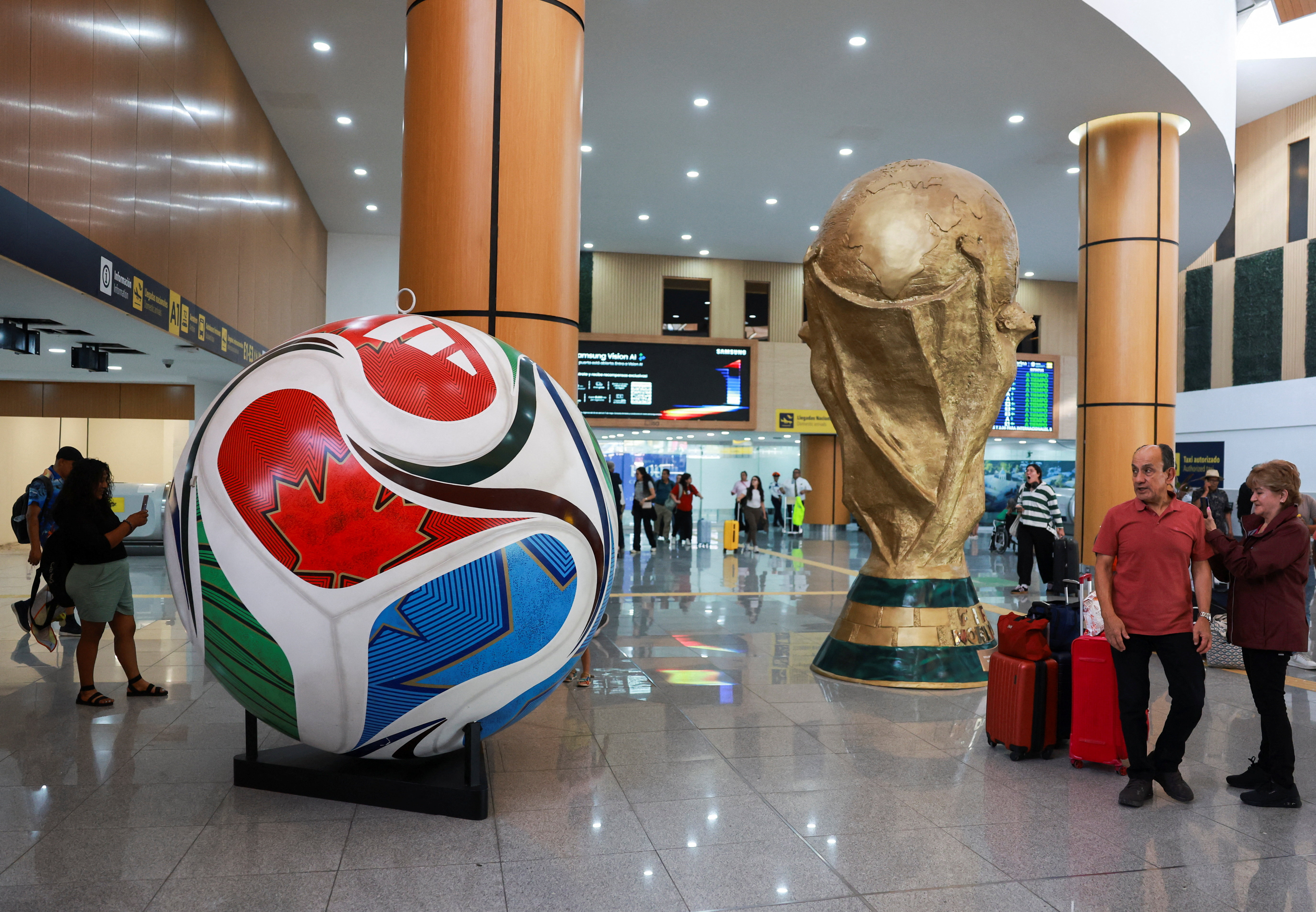 Passengers look at a giant model of the football called and a replica of the World Cup trophy as we look at the expected legal betting handle for the upcoming 2026 FIFA World Cup.