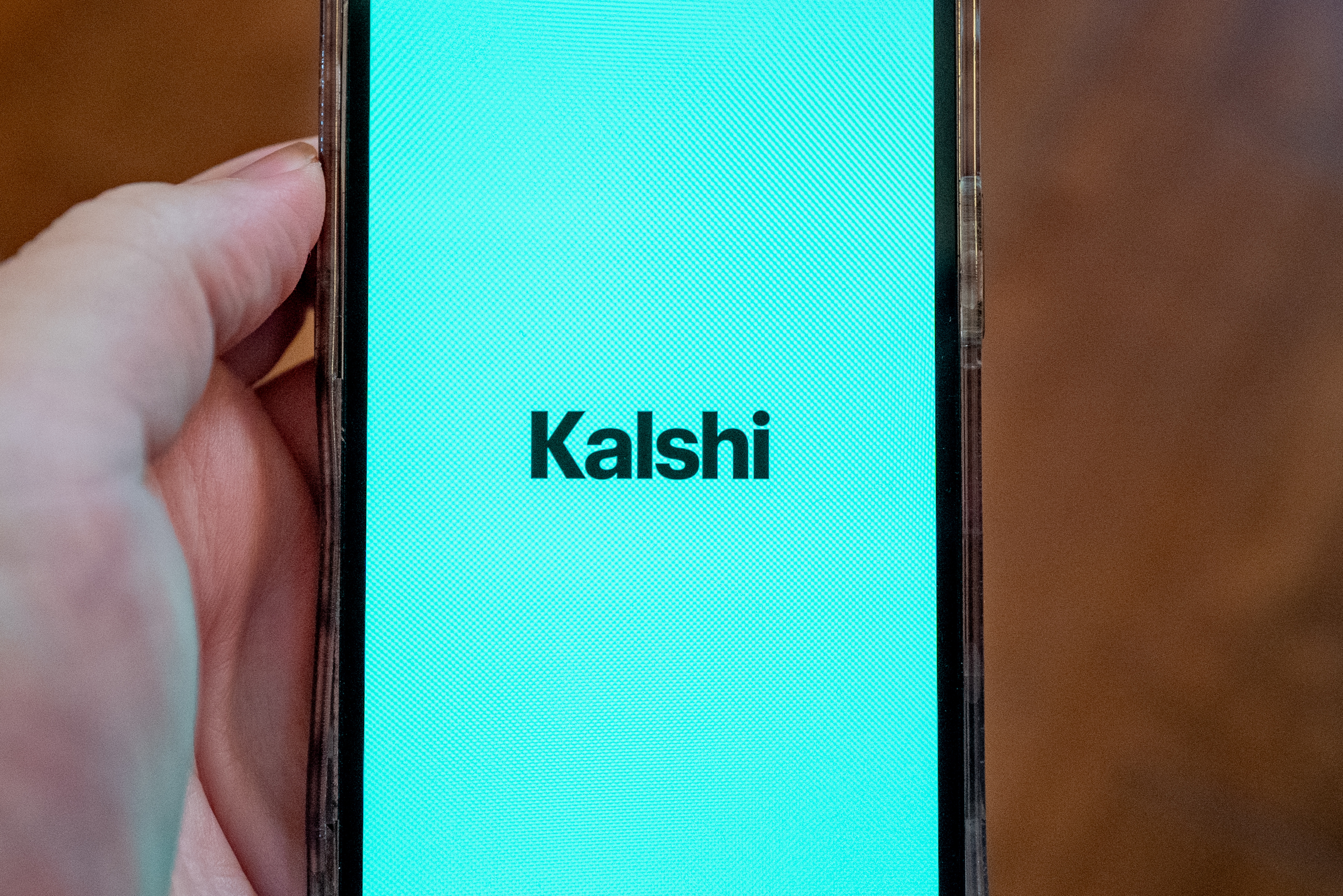 A person's hand holding a smartphone displaying the Kalshi app's opening screen as we look at the Sixth Circuit's ruling against the prediction market app.