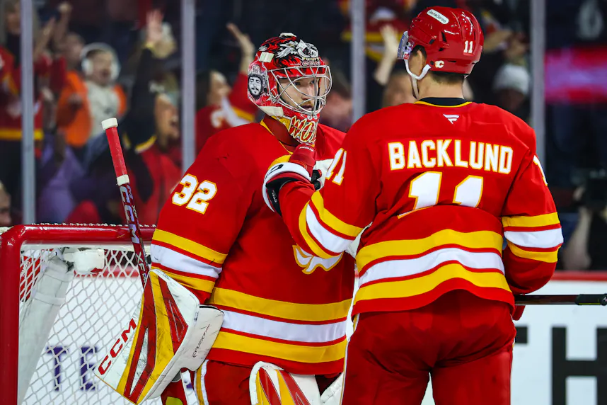 Calgary Flames goaltender Dustin Wolf and center Mikael Backlund celebrate win after defeating Florida Panthers at Scotiabank Saddledome as we look at our Bruins vs. Flames prediction.