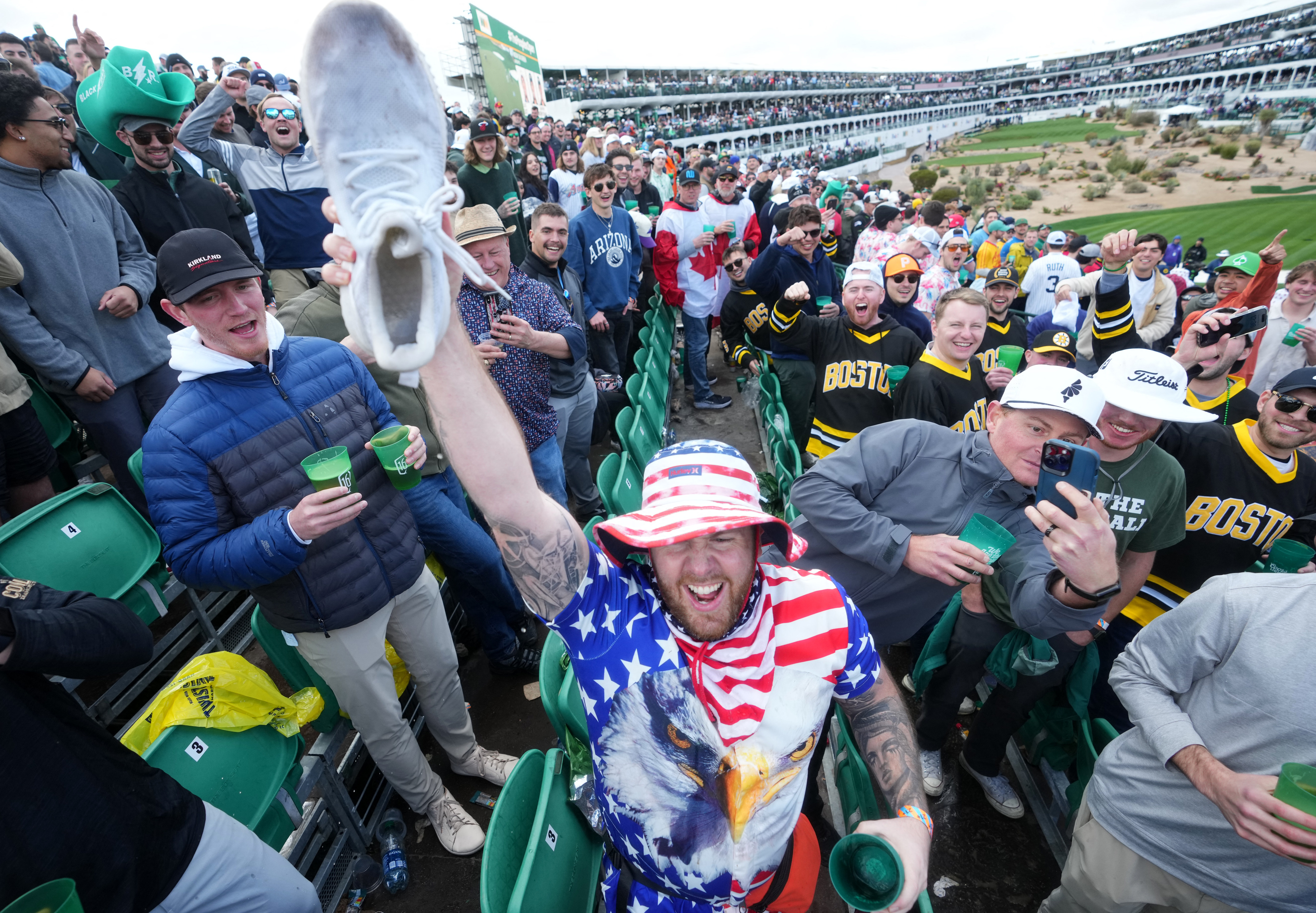 Fans drink from a shoe in the stands on the 16th hole during the WM Phoenix Open at TPC Scottsdale